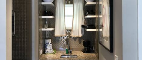 A modern kitchen with white cabinets, a granite countertop, a coffee maker, and a hanging light fixture.