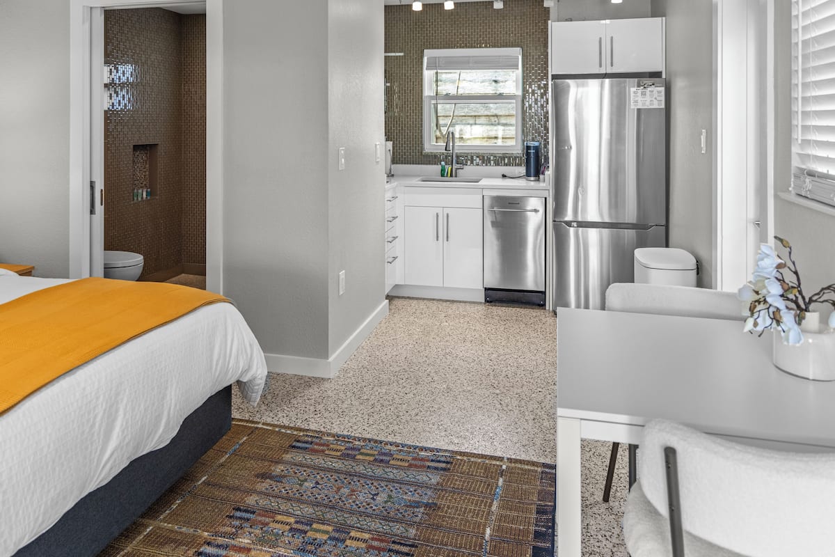 A modern bedroom with a large bed, a bathroom with a shower, and a kitchen with a refrigerator and sink.