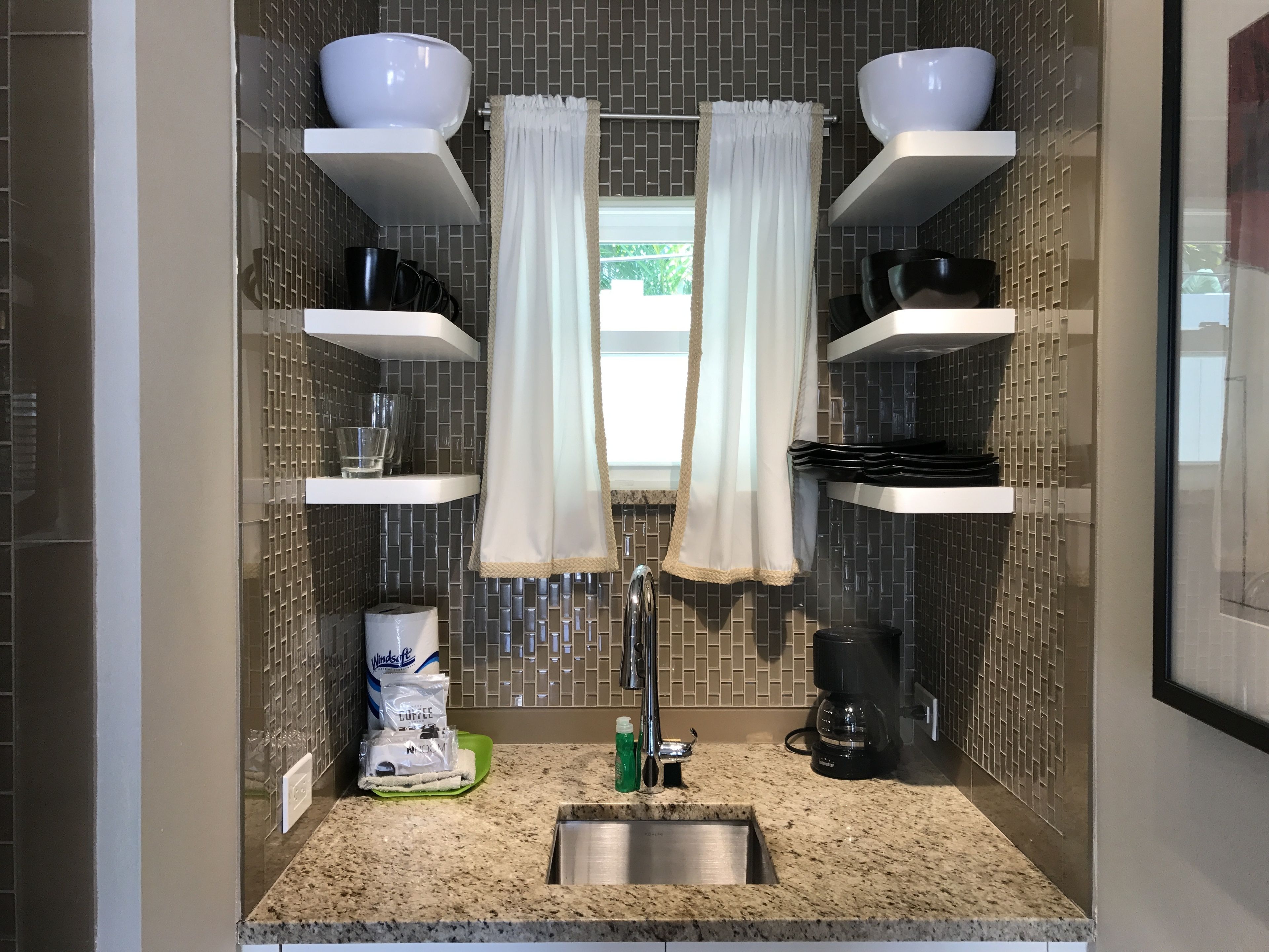 A modern bathroom with a granite countertop, a sink, a coffee maker, and a shower curtain.