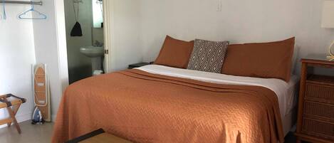 Un dormitorio con cama, mesita de noche, una silla y una pequeña mesa.