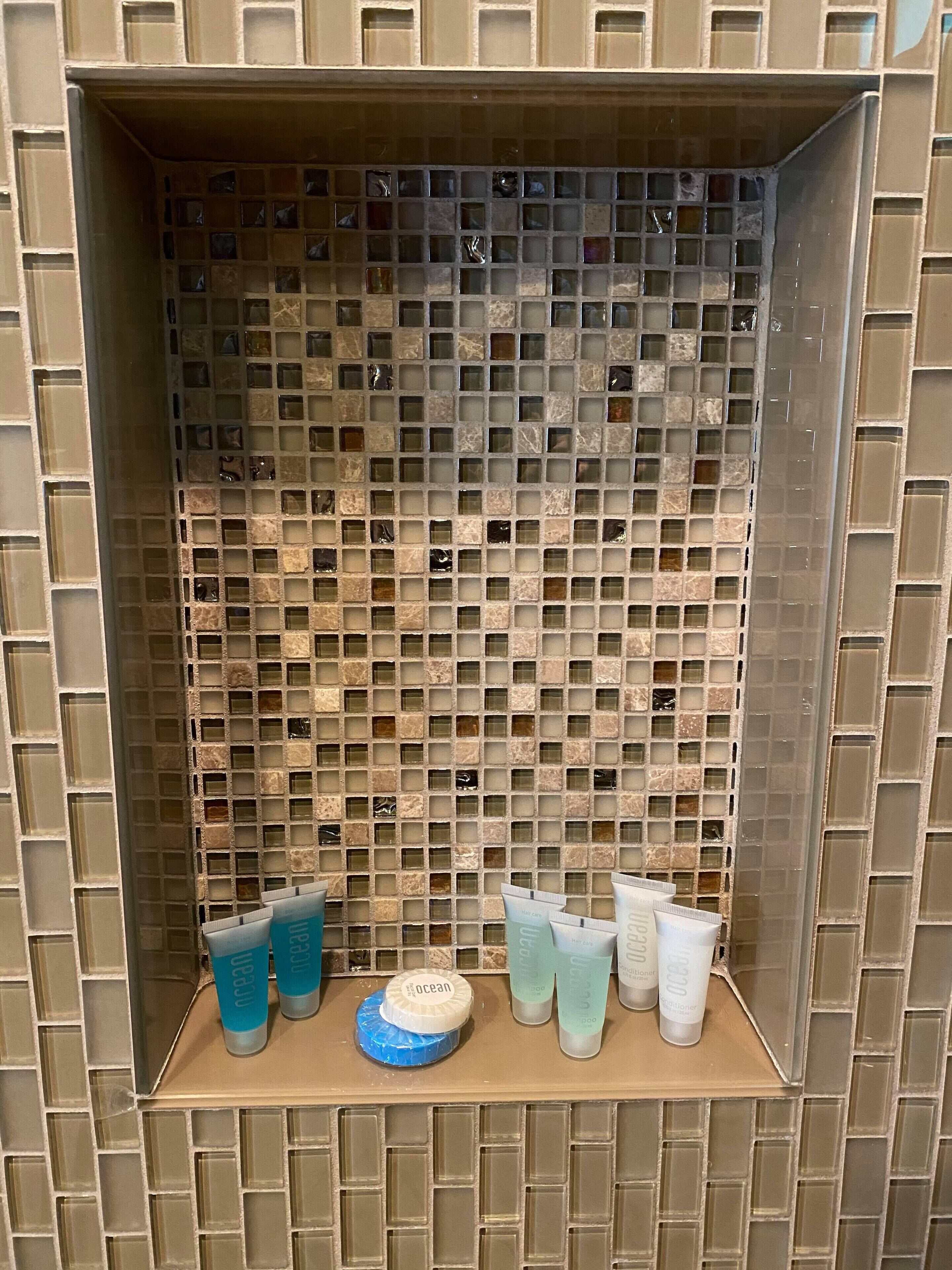 A bathroom with a mosaic tile wall and a shelf with various toiletries.