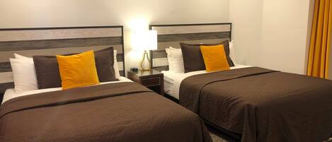 A hotel room with two beds, each with a brown bedspread and pillows, a bedside table with a lamp, and a wooden headboard.