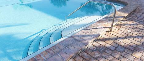 A swimming pool with a metal handrail and a brick border.