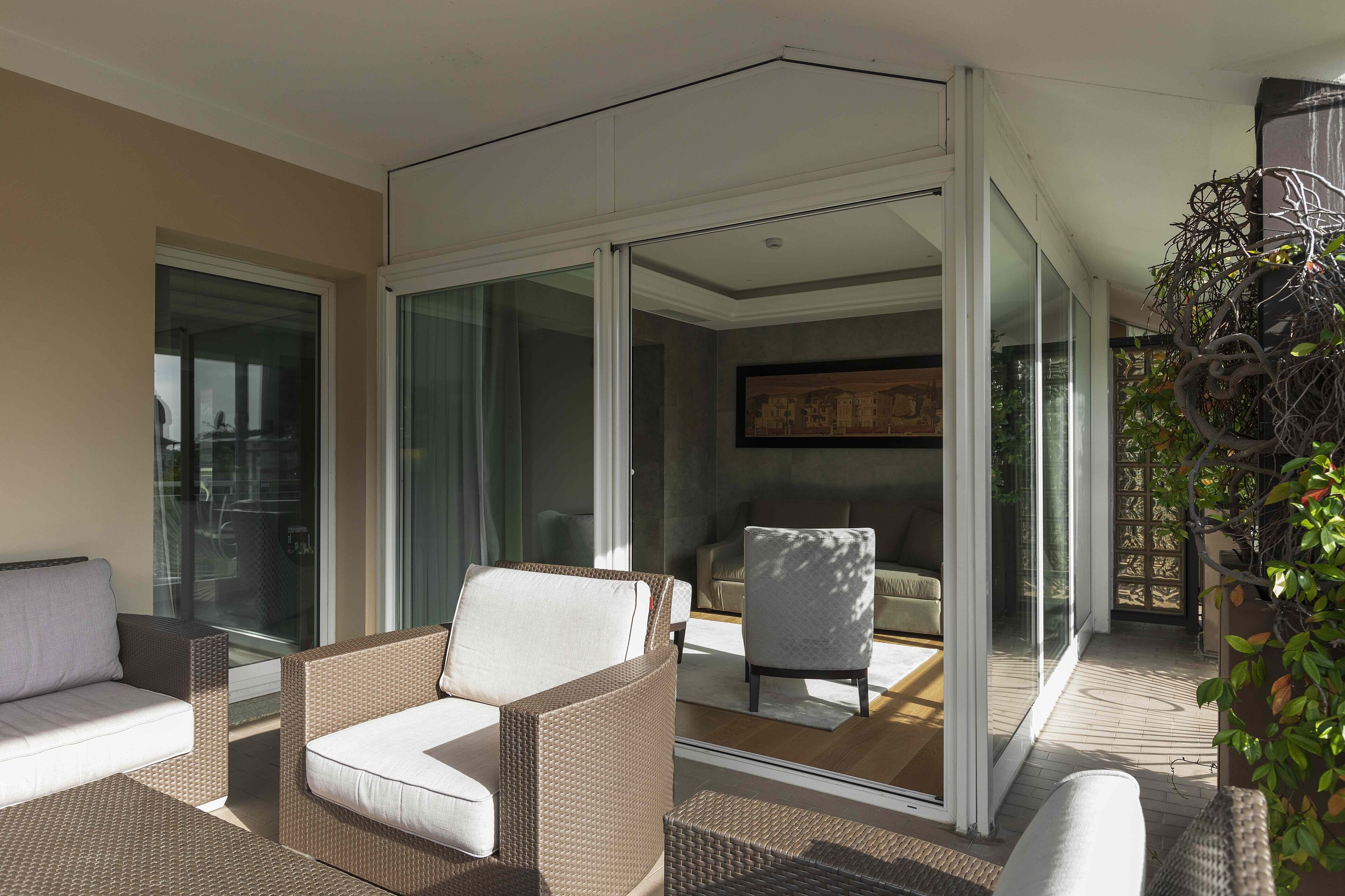 A modern living area with wicker furniture, a glass door leading to a balcony, and a framed artwork on the wall.