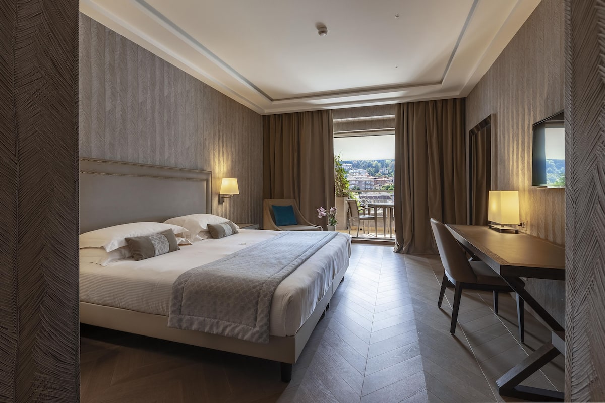 Ein Hotelzimmer mit einem großen Bett, einem Schreibtisch und Blick auf die Stadt.