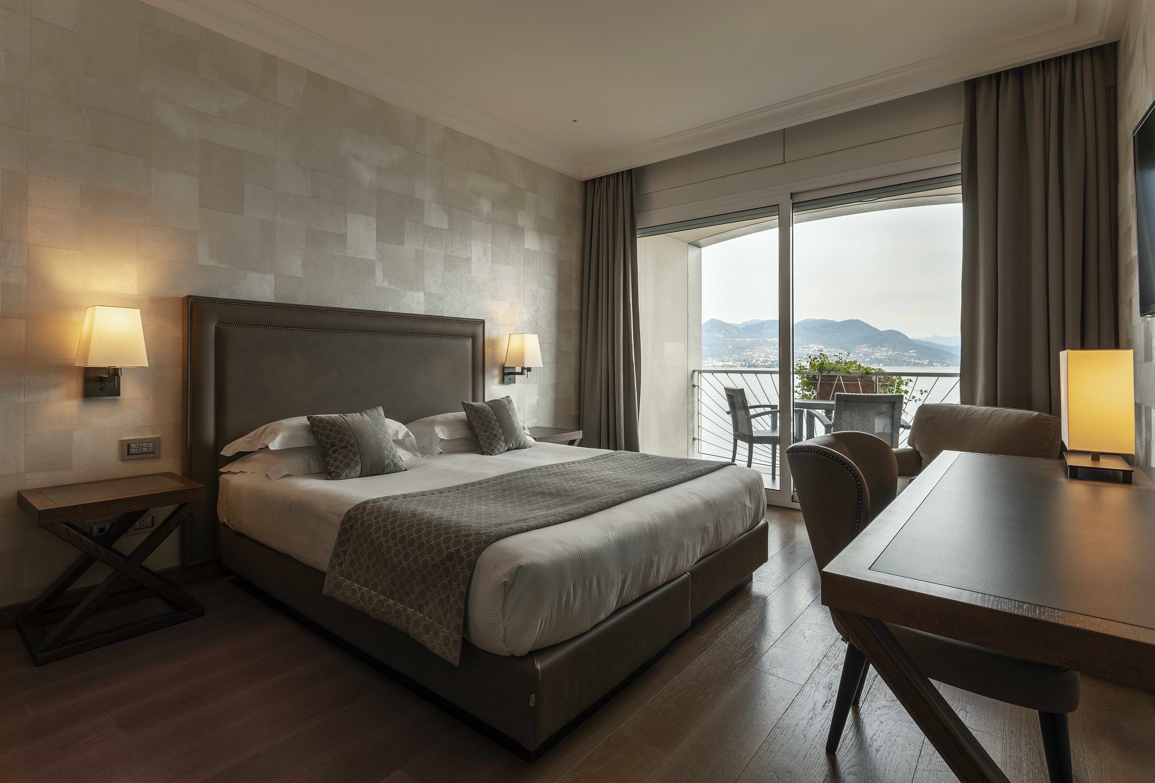 Habitación de hotel con una cama grande, una mesa de comedor y vistas de la ciudad a través de amplias ventanas.