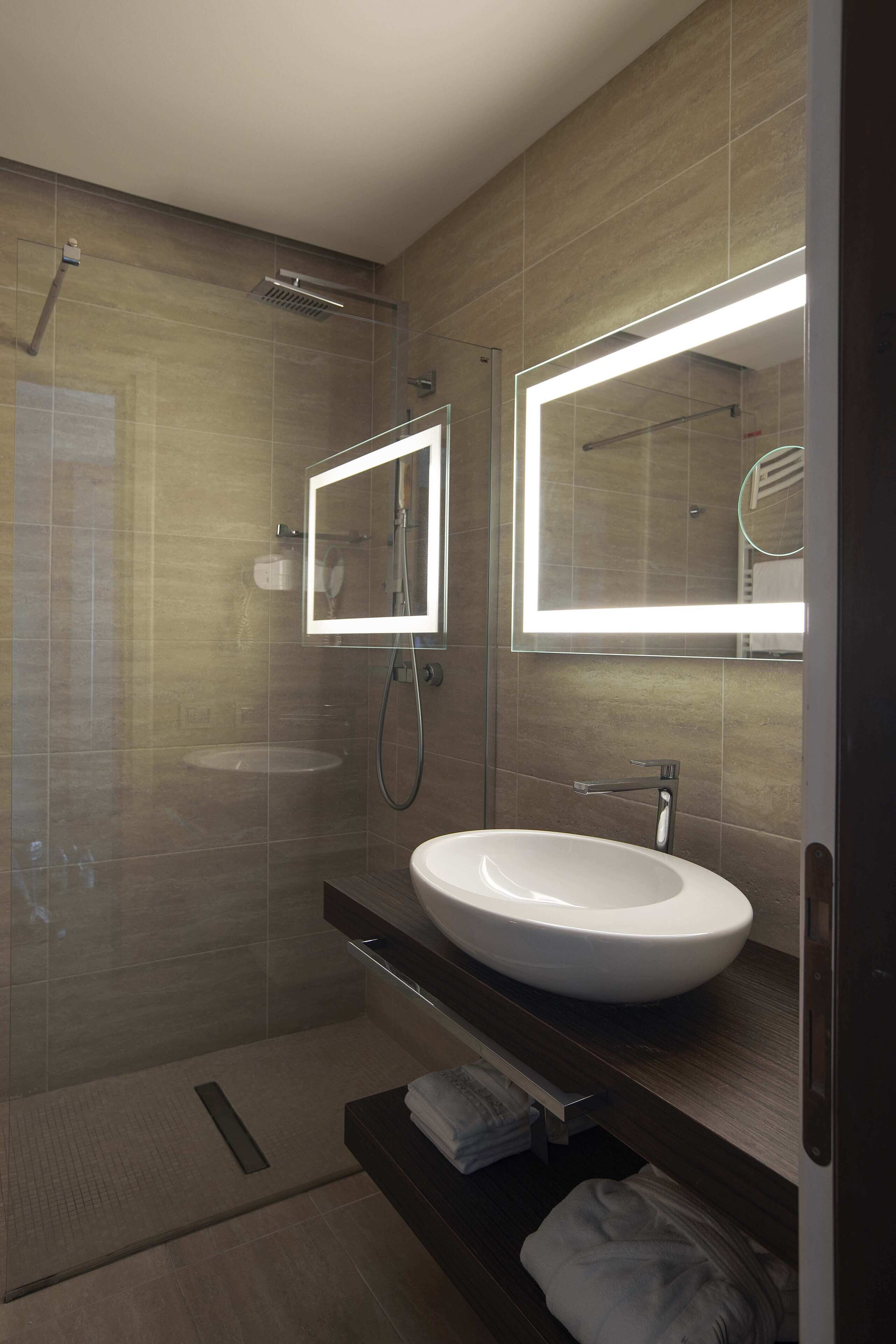 A modern bathroom with a glass-enclosed shower, a white sink, and a mirror with integrated lighting.