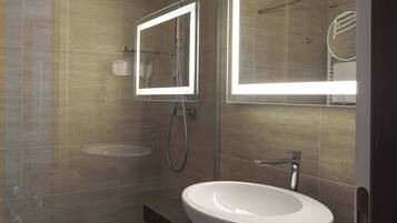 A modern bathroom with a glass-enclosed shower, a white sink, and a mirror with integrated lighting.