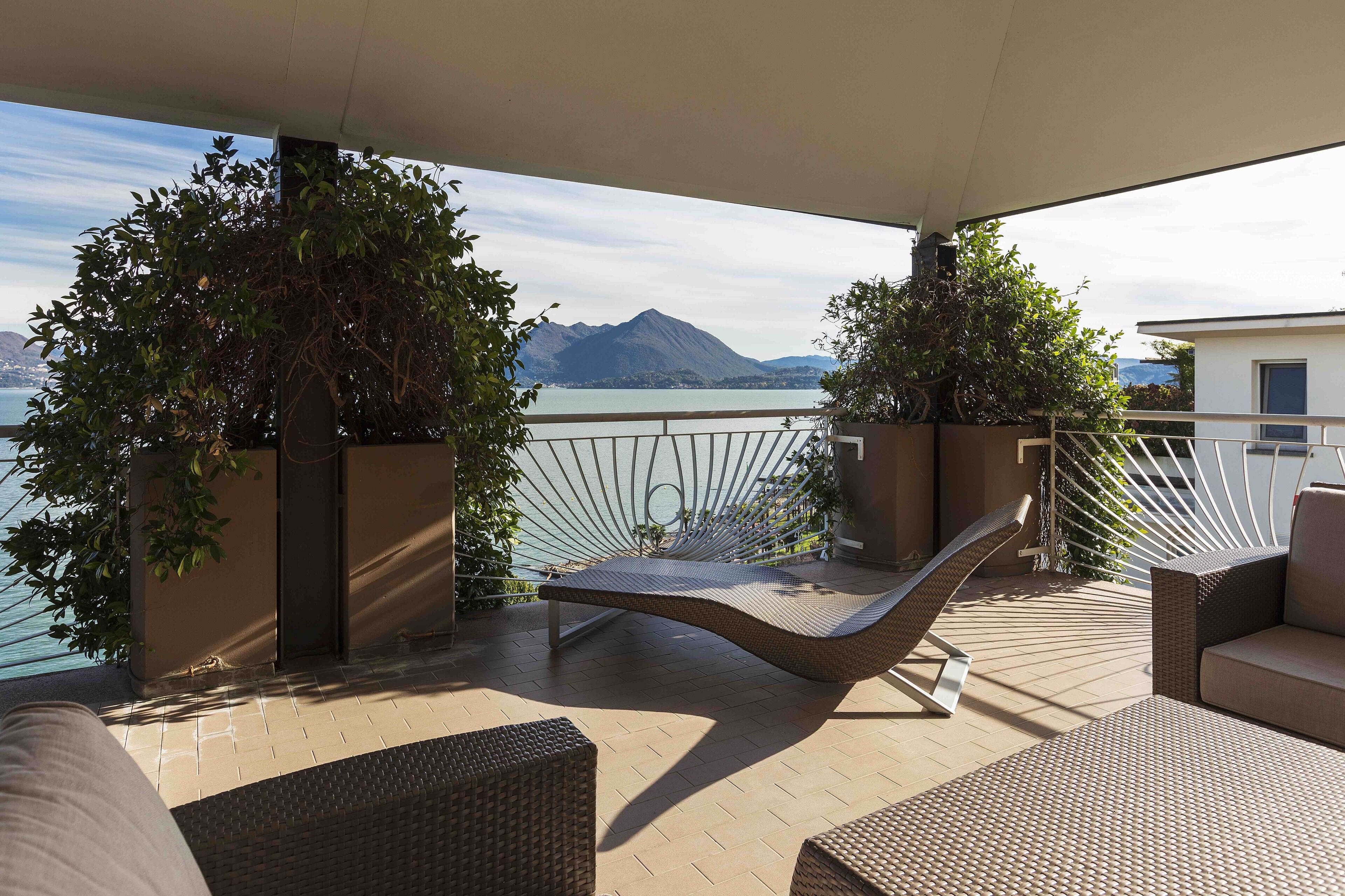 A balcony with wicker furniture, a view of a mountain, and a body of water.