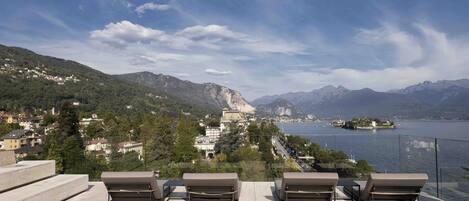 A terrace with lounge chairs overlooking a scenic lake and mountains.