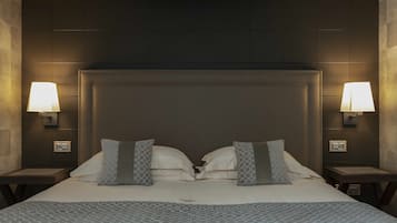 Un lit bien fait, recouvert d’une couvre-lit à motifs, avec deux oreillers et une tête de lit. On y trouve deux tables de chevet avec des lampes et un panneau de commande fixé au mur.