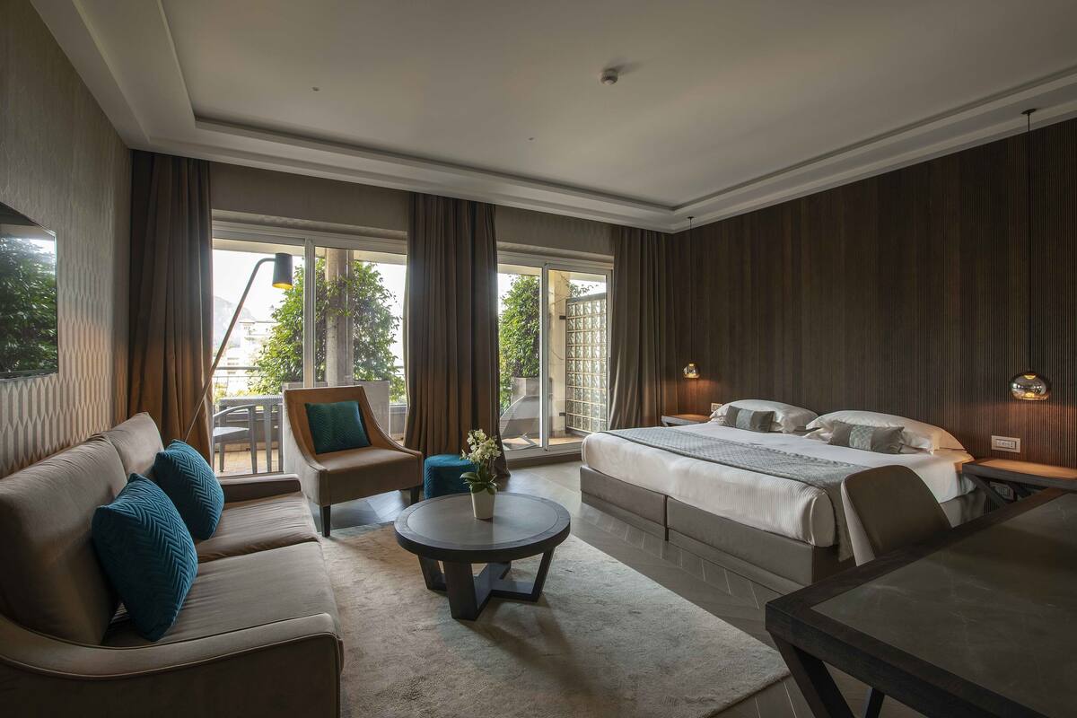 Ein modernes Hotelzimmer mit einem großen Bett, einem Sofa, einem runden Couchtisch und einem Esstisch.