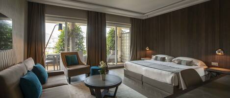 A modern hotel room with a large bed, a sofa, a round coffee table, and a dining table.