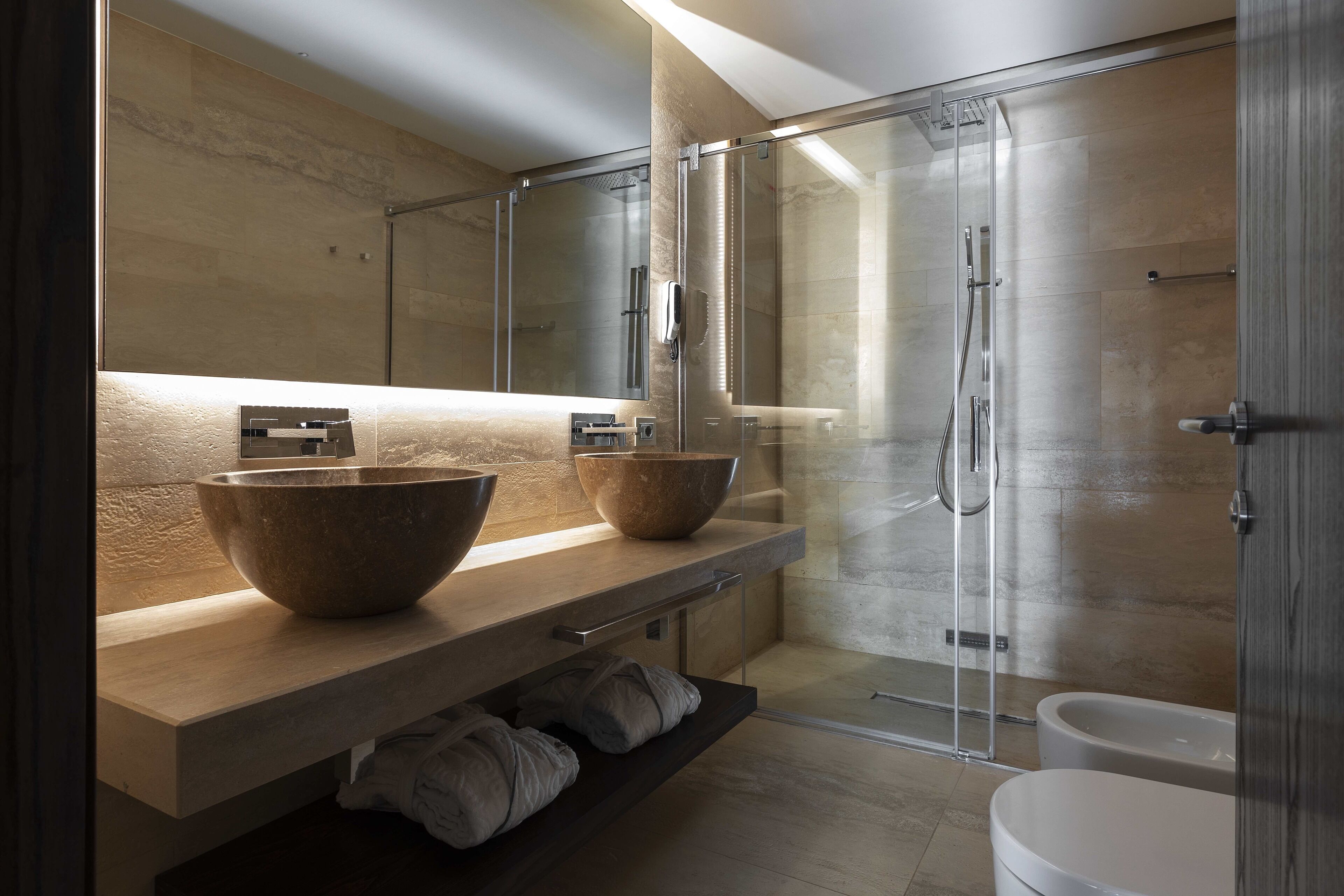 A modern bathroom with a large mirror, two large bowls on the vanity, a glass shower enclosure, and a white toilet.