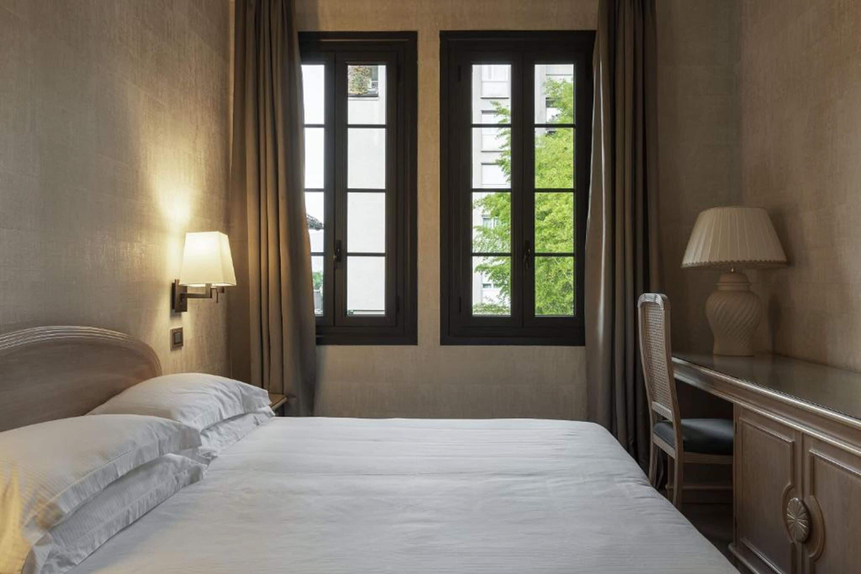Ein Hotelzimmer mit Bett, zwei Fenstern, Schreibtisch und Stuhl.