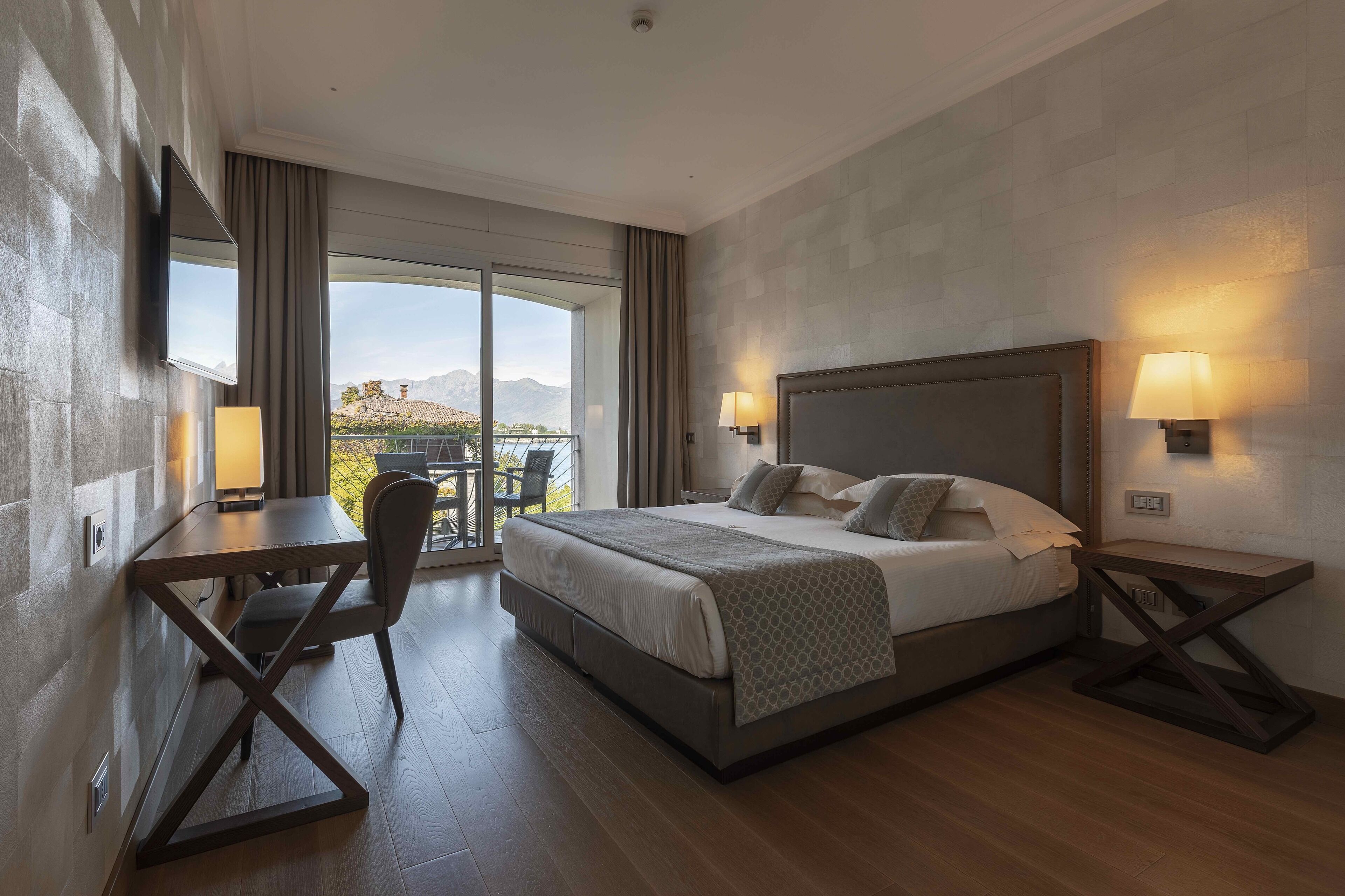 Ein modernes Hotelzimmer mit einem großen Bett, einem Schreibtisch und einem Sessel. Ein Balkon bietet Blick auf die Berge.