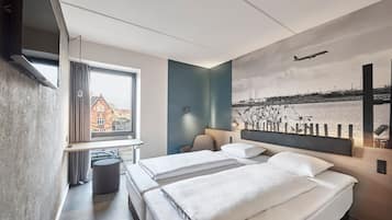 Ein Hotelzimmer mit zwei Betten, einem Fernseher, einem Fenster mit Vorhängen, einer Lampe und einem Wandbild einer Brücke und eines Flusses.