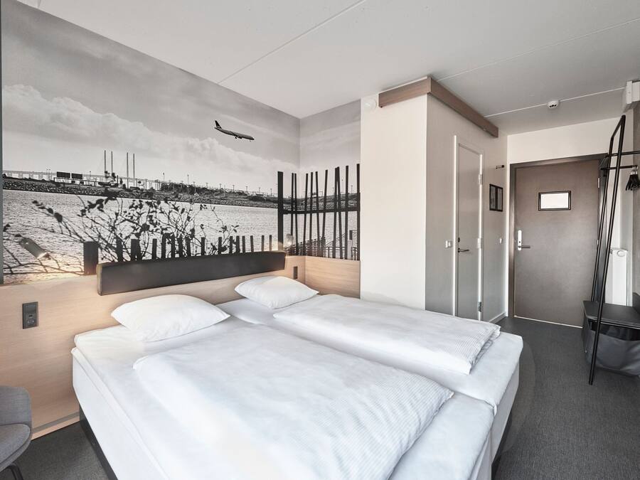 Une chambre d’hôtel moderne avec un grand lit, un bureau et une fresque murale représentant un paysage de bord de mer.