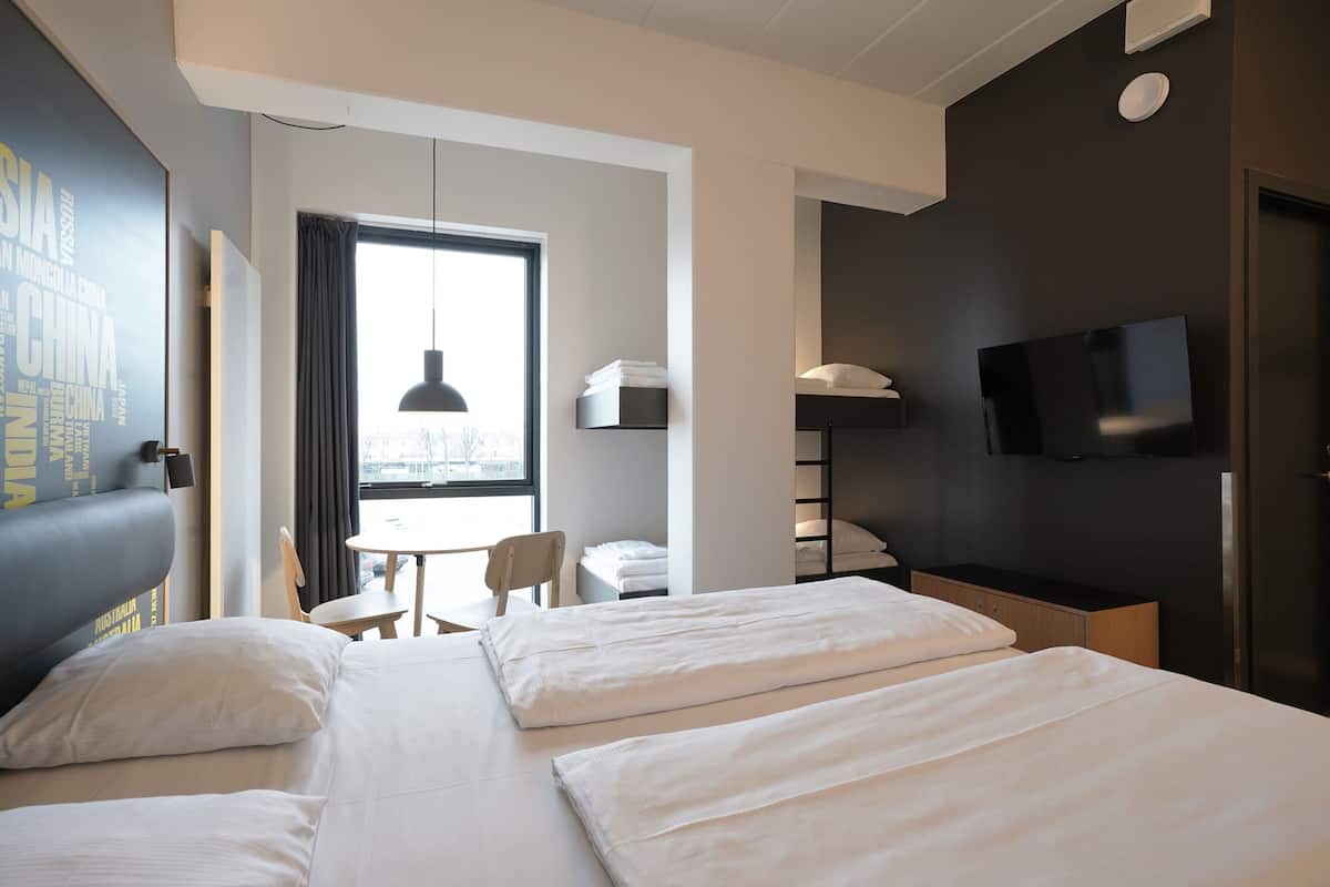 Une chambre d’hôtel avec deux lits, une télévision, un bureau et une fenêtre avec des rideaux.