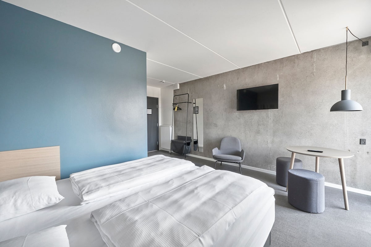 Une chambre d’hôtel moderne, dotée d’un grand lit, d’un bureau, d’une chaise et d’un téléviseur fixé au mur.