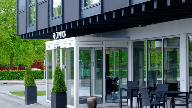 A reception area with a glass door entrance, outdoor seating with chairs and tables, and a potted plant. - Four Points Flex by Sheraton Copenhagen Airport (Kastrup)