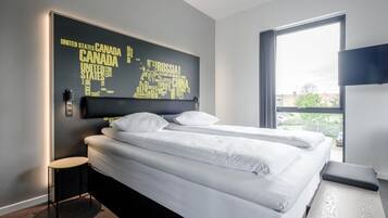 Ein Hotelzimmer mit Bett, einem kleinen Hocker, einem Tisch und einem großen Fenster.