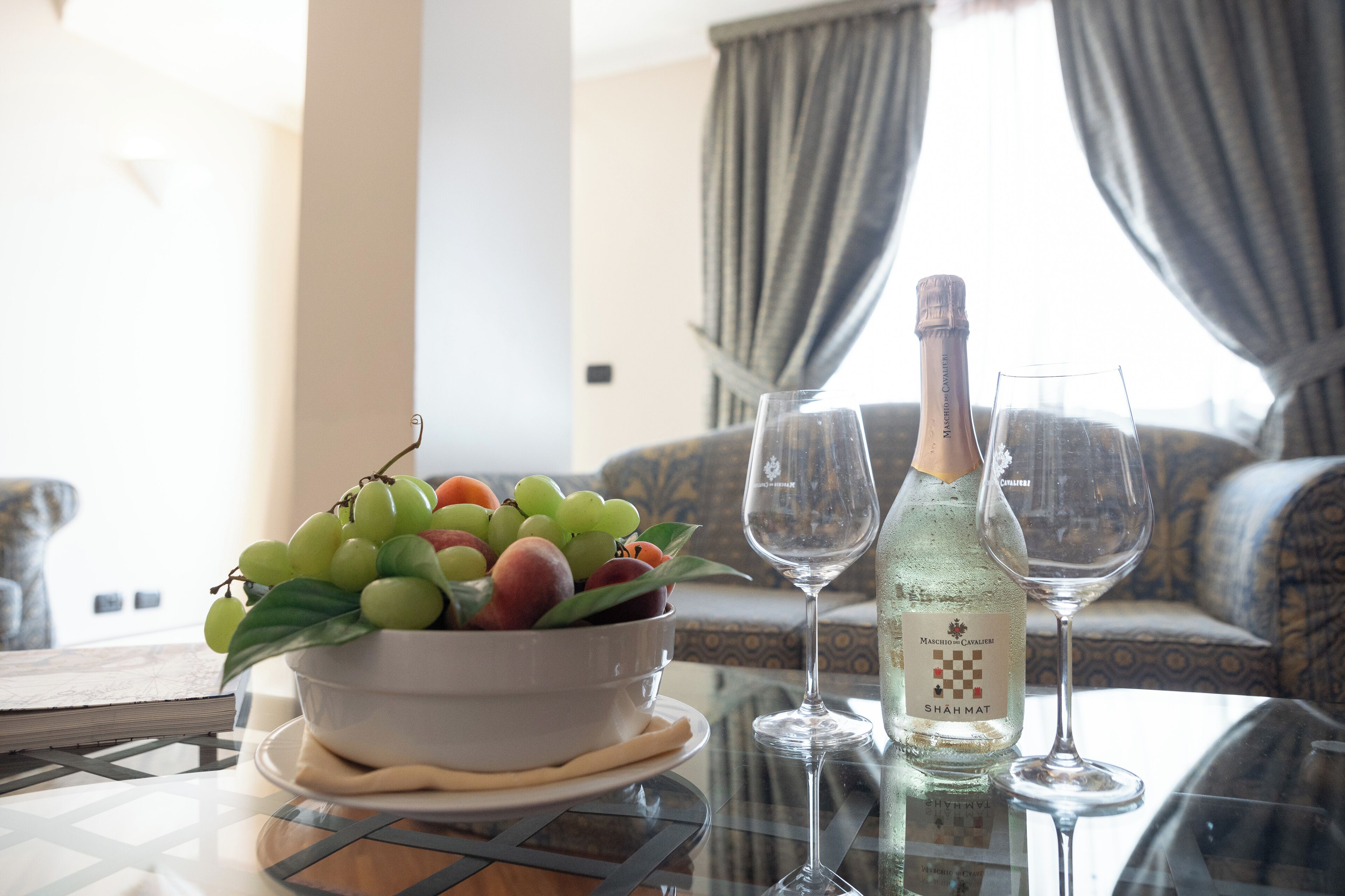 A table with a bowl of fruit, a bottle of wine, and two wine glasses.