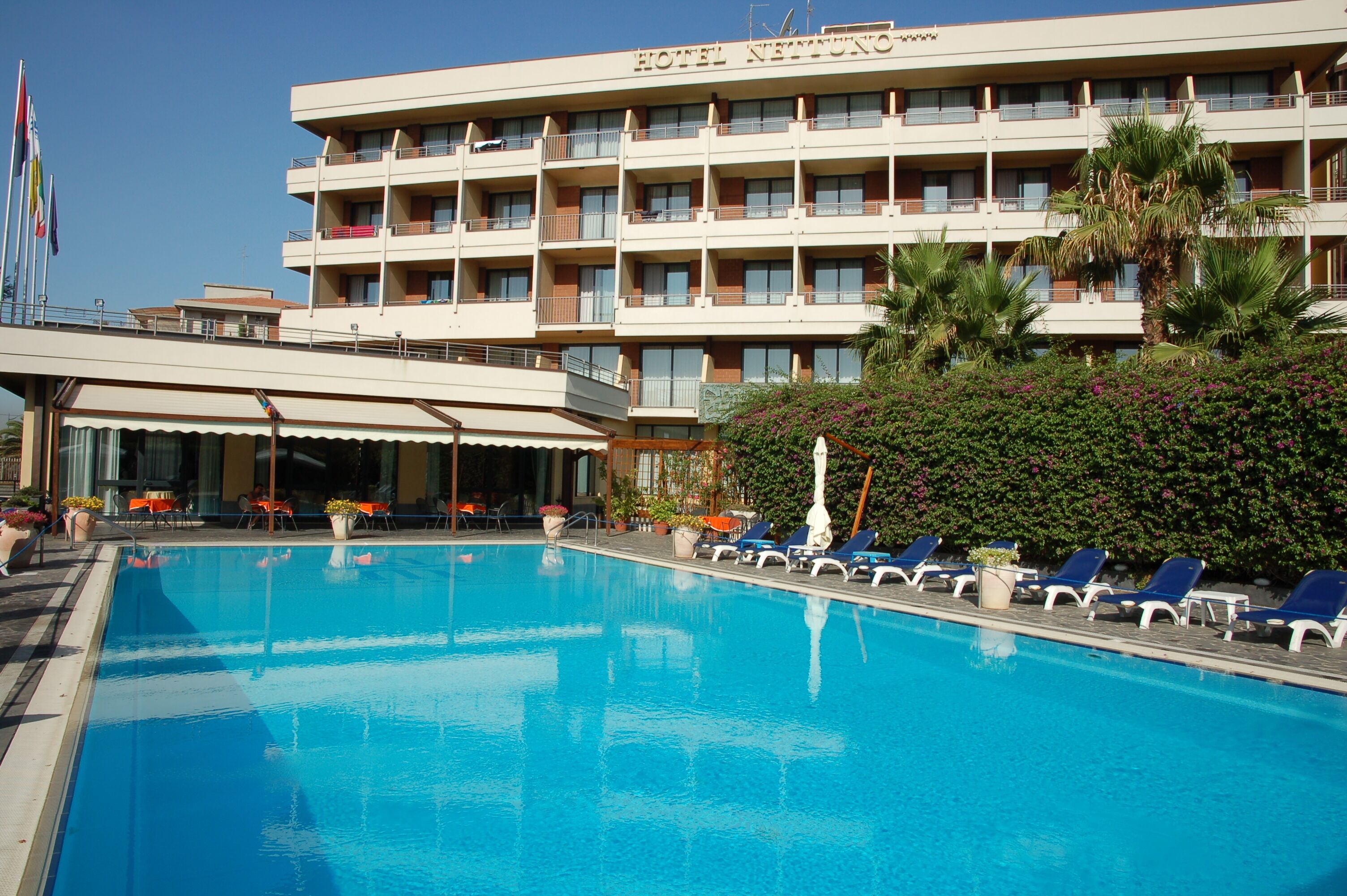 A hotel with a swimming pool, sun loungers, and a covered area with tables and chairs.
