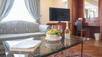 Una sala de estar con un sofá, una mesa de centro de cristal con un frutero y una botella, un televisor y una zona de comedor de madera.