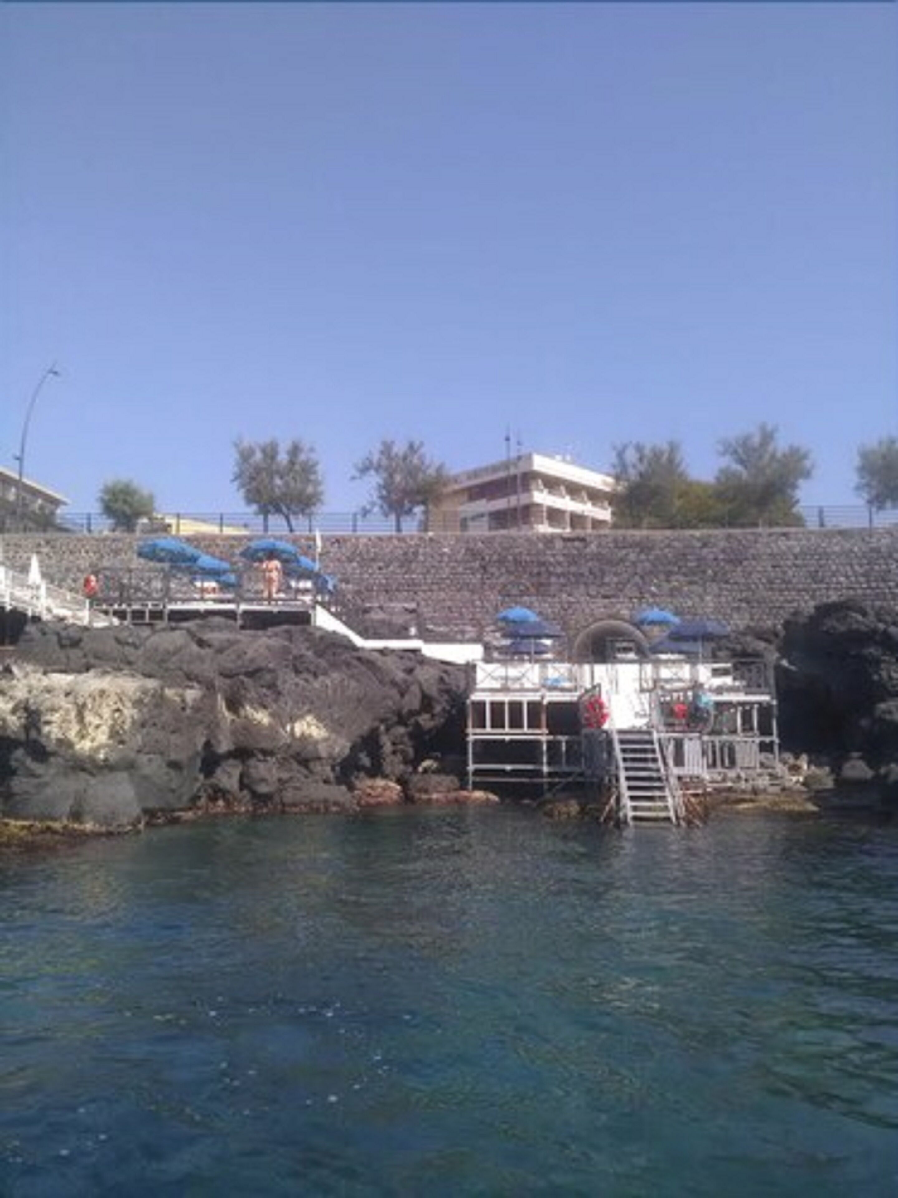 Edificio sul lungomare con muro in pietra, area piscina e posto di salvataggio.