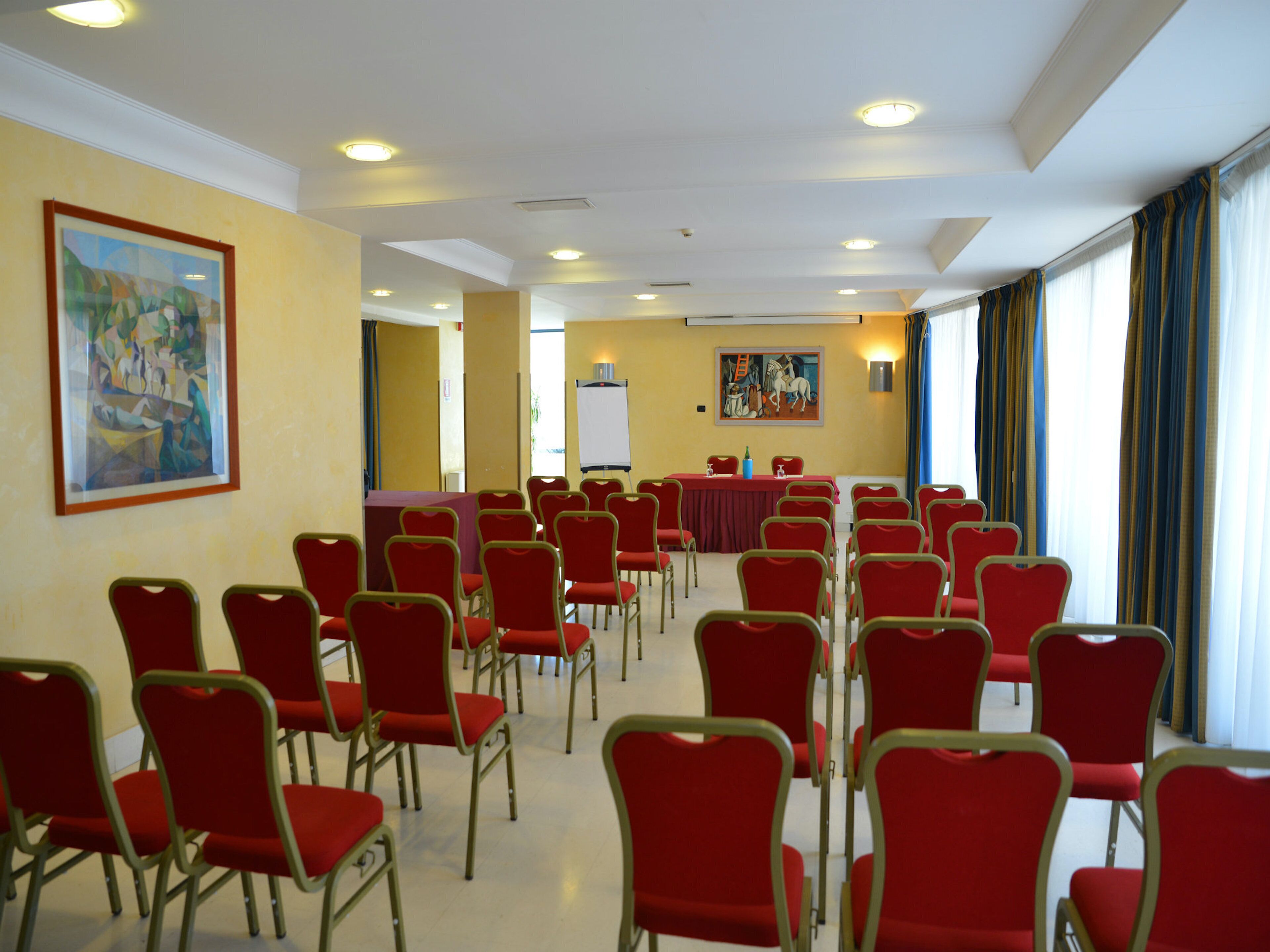 Una sala conferenze con file di sedie rosse, un lungo tavolo e una lavagna.