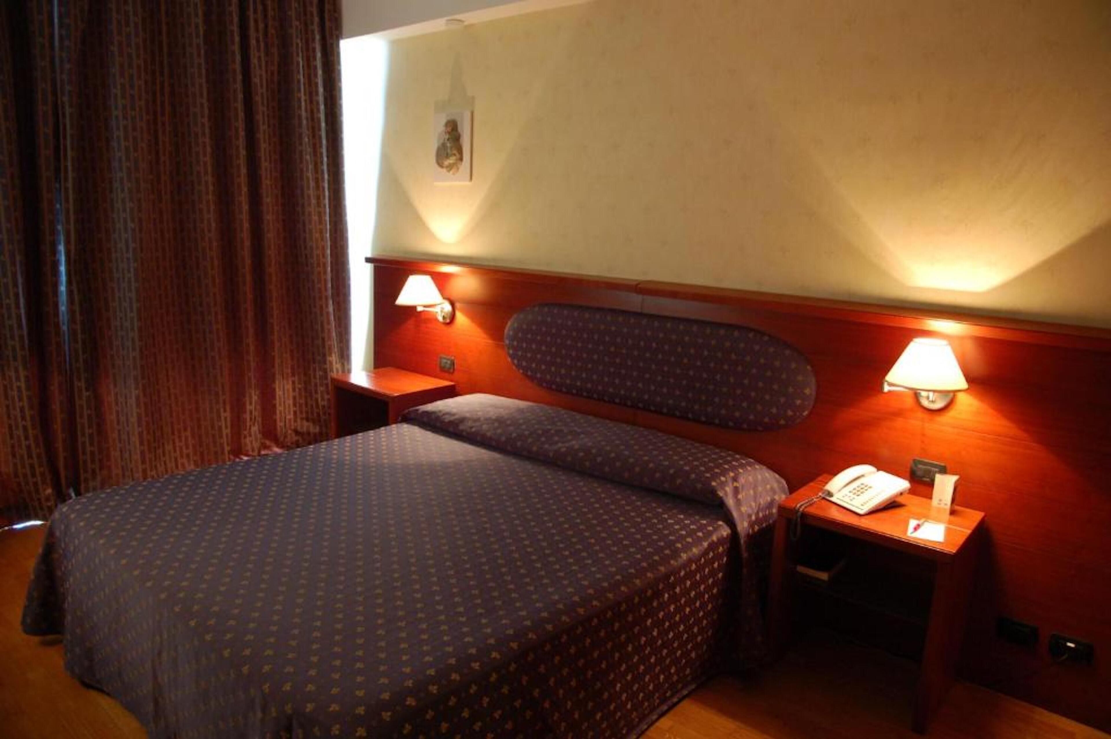 Quarto de hotel com cama, duas mesas de cabeceira e duas luminárias de parede.