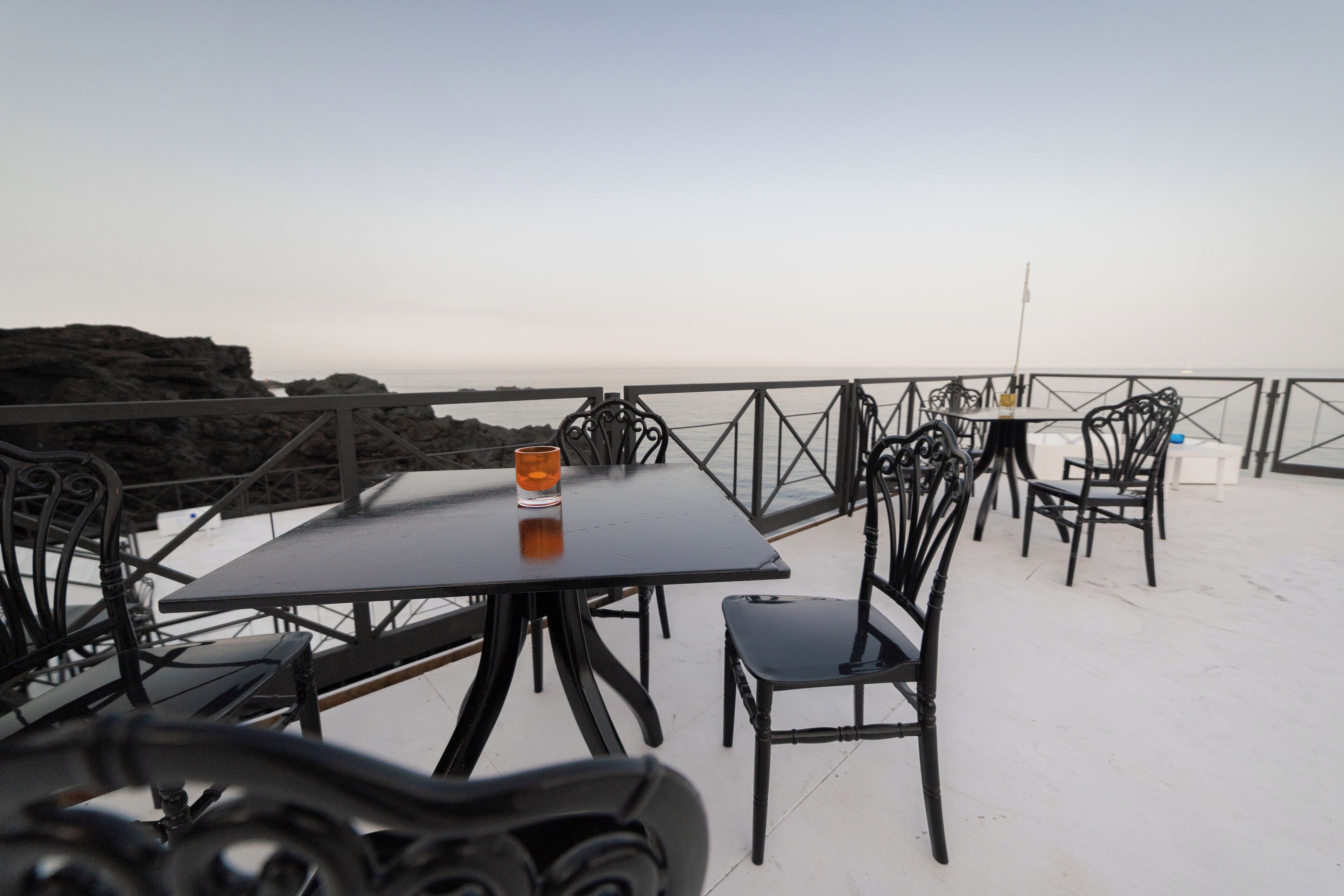 A terrace with tables and chairs, overlooking a rocky coastline.