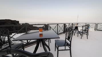 Una terraza con mesas y sillas, con vistas a un escarpado litoral.