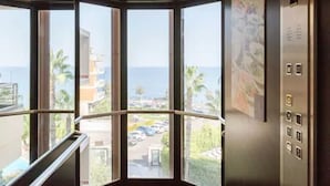 A corner view of an elevator with large windows offering a view of a parking lot and buildings. - Hotel Nettuno (Catania)