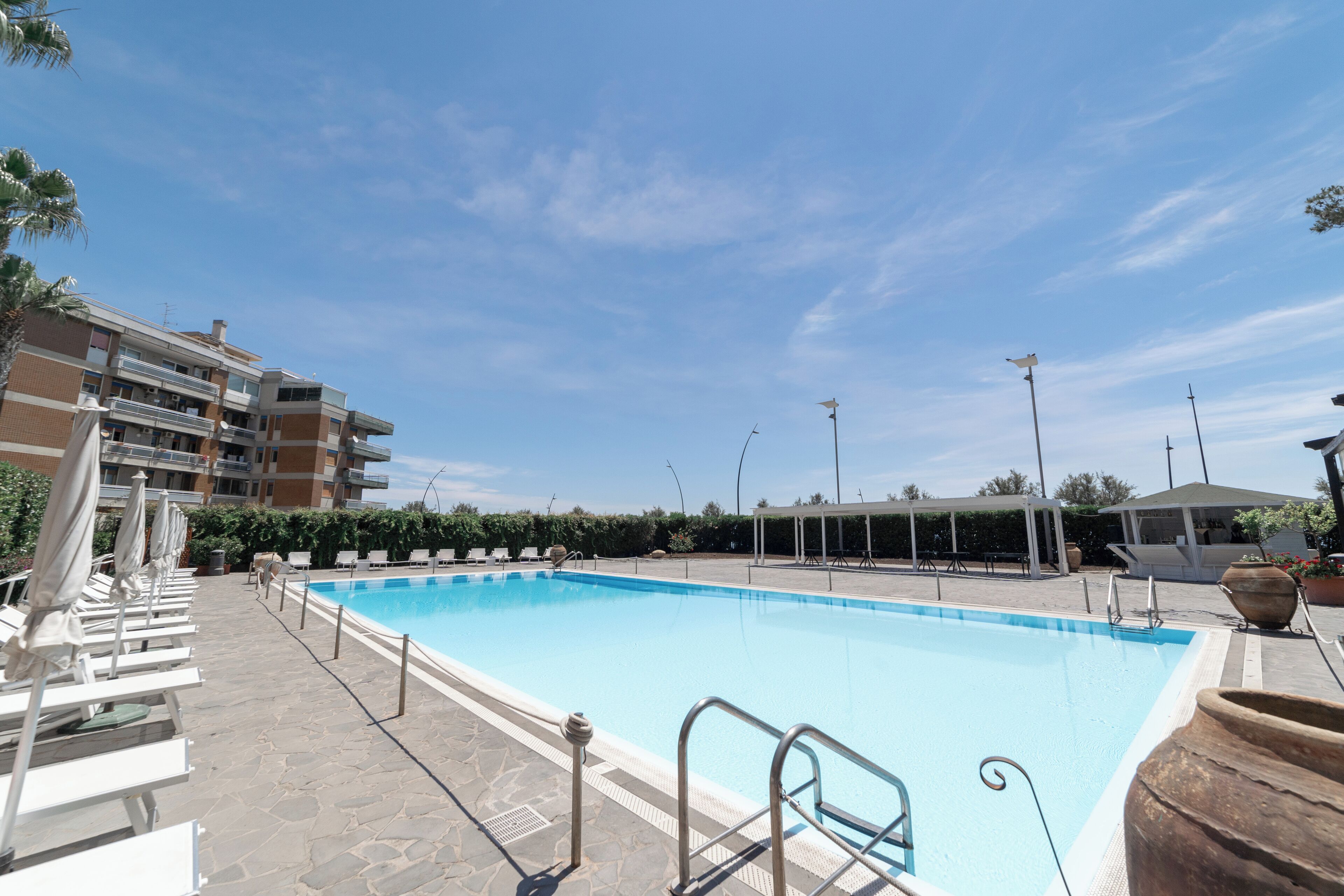 A swimming pool with lounge chairs and umbrellas, surrounded by a multi-story building.
