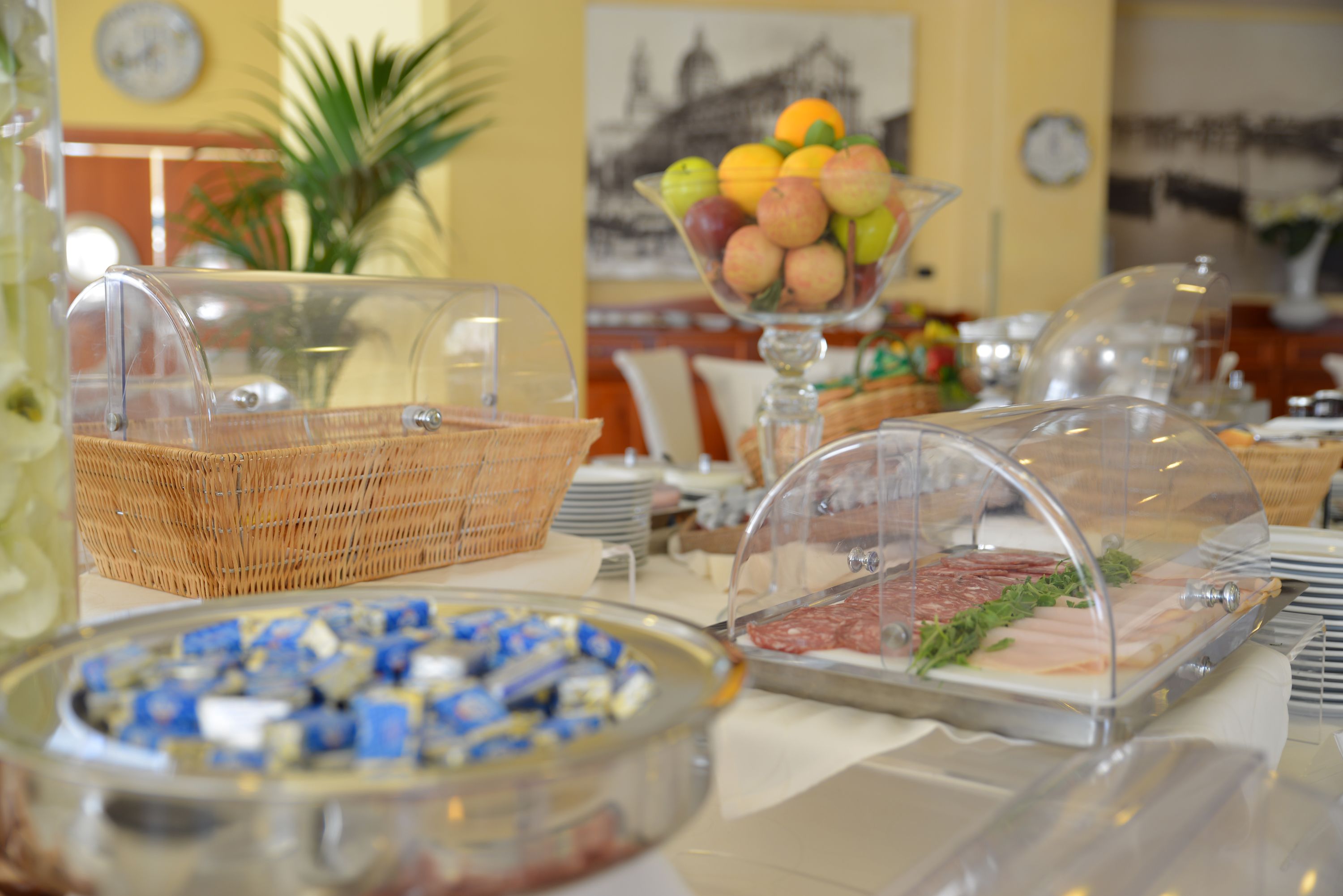 Un bufé con diversos alimentos, incluyendo un bol de vidrio con fruta, una cesta de mimbre y una presentación de carnes.