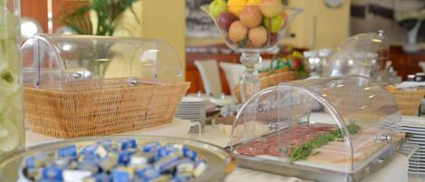 Un bufé con diversos alimentos, incluyendo un bol de vidrio con fruta, una cesta de mimbre y una presentación de carnes.
