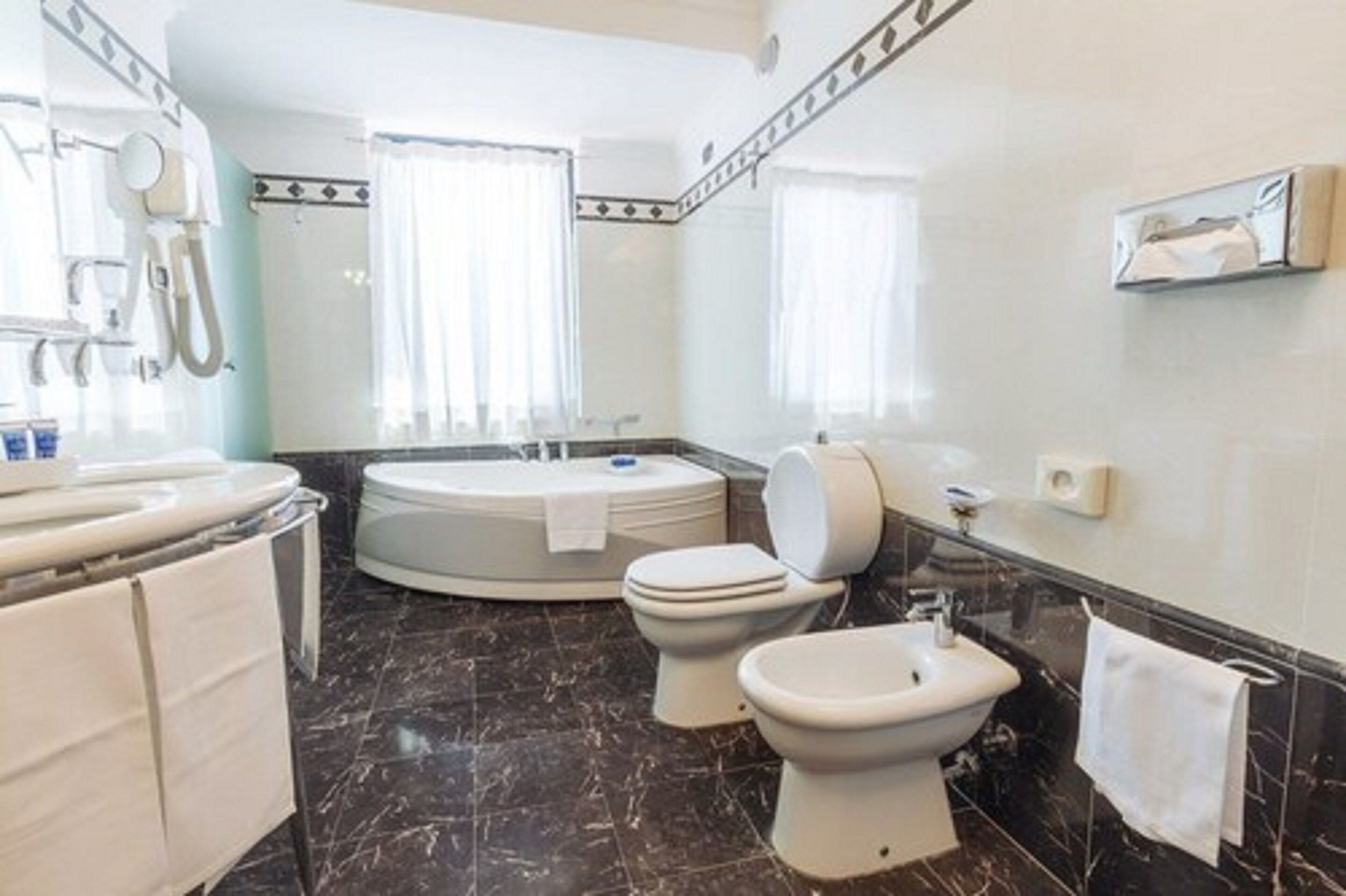 A modern bathroom with a bathtub, toilet, bidet, and a vanity with a mirror.