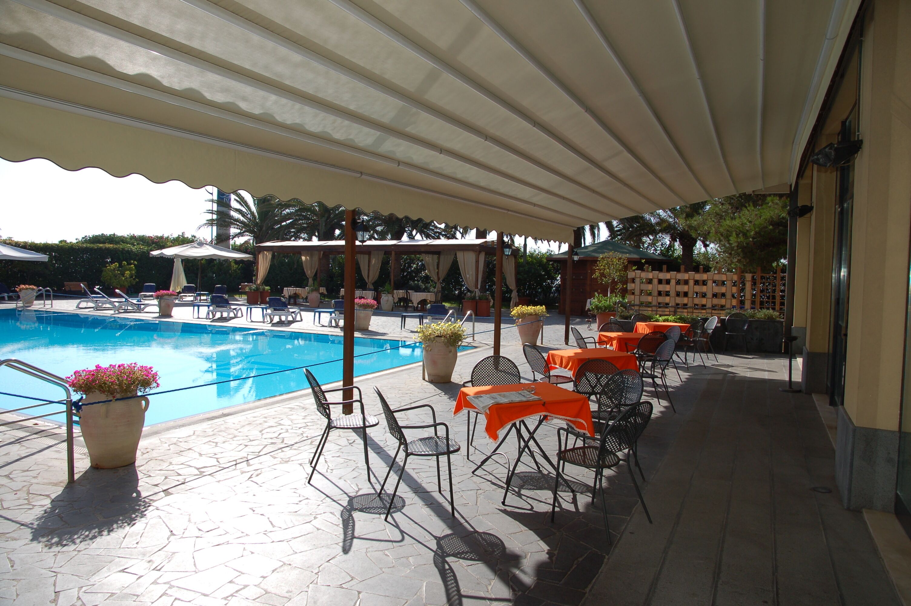 Ein überdachter Außenbereich mit Pool, Liegestühlen und Tischen.