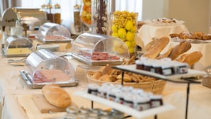 A buffet table with various food items, including meats, breads, and pastries, covered with clear domes. - Hotel Nettuno (Catania)