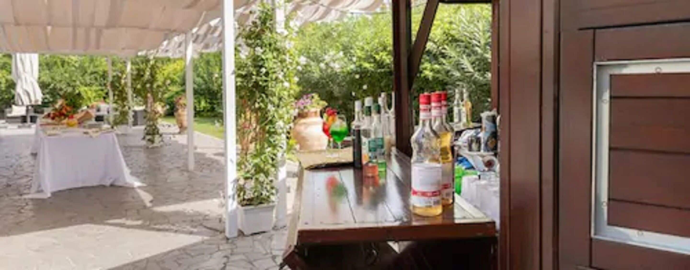 An outdoor bar area with a table set up under a canopy, surrounded by greenery.