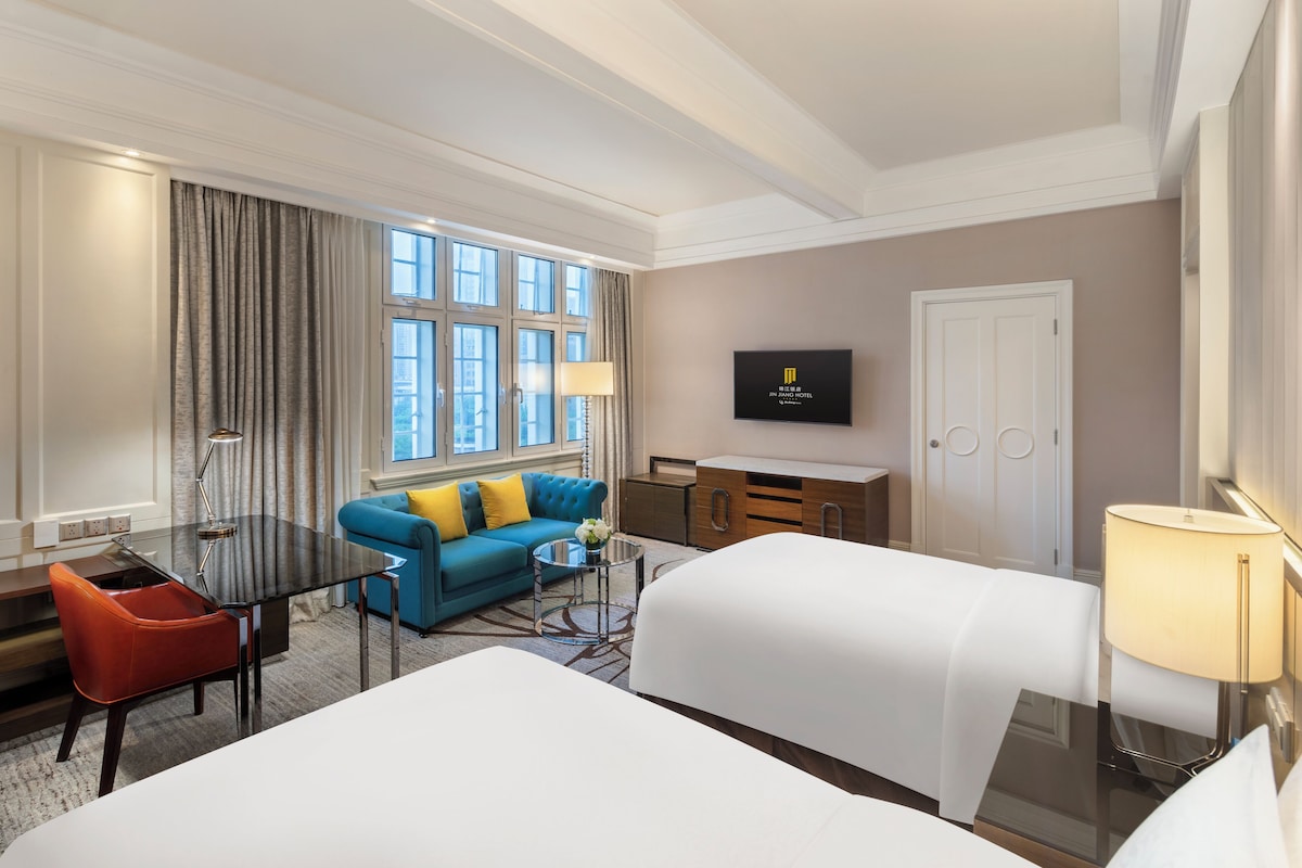 Een hotelkamer met een groot bed, een bank, een bureau met stoel, een televisie en een raam met gordijnen.