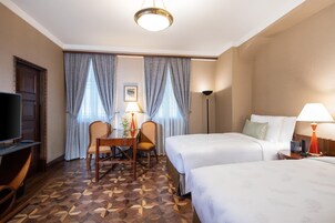 A hotel room with two beds, a desk with a chair, a television, and a lamp.