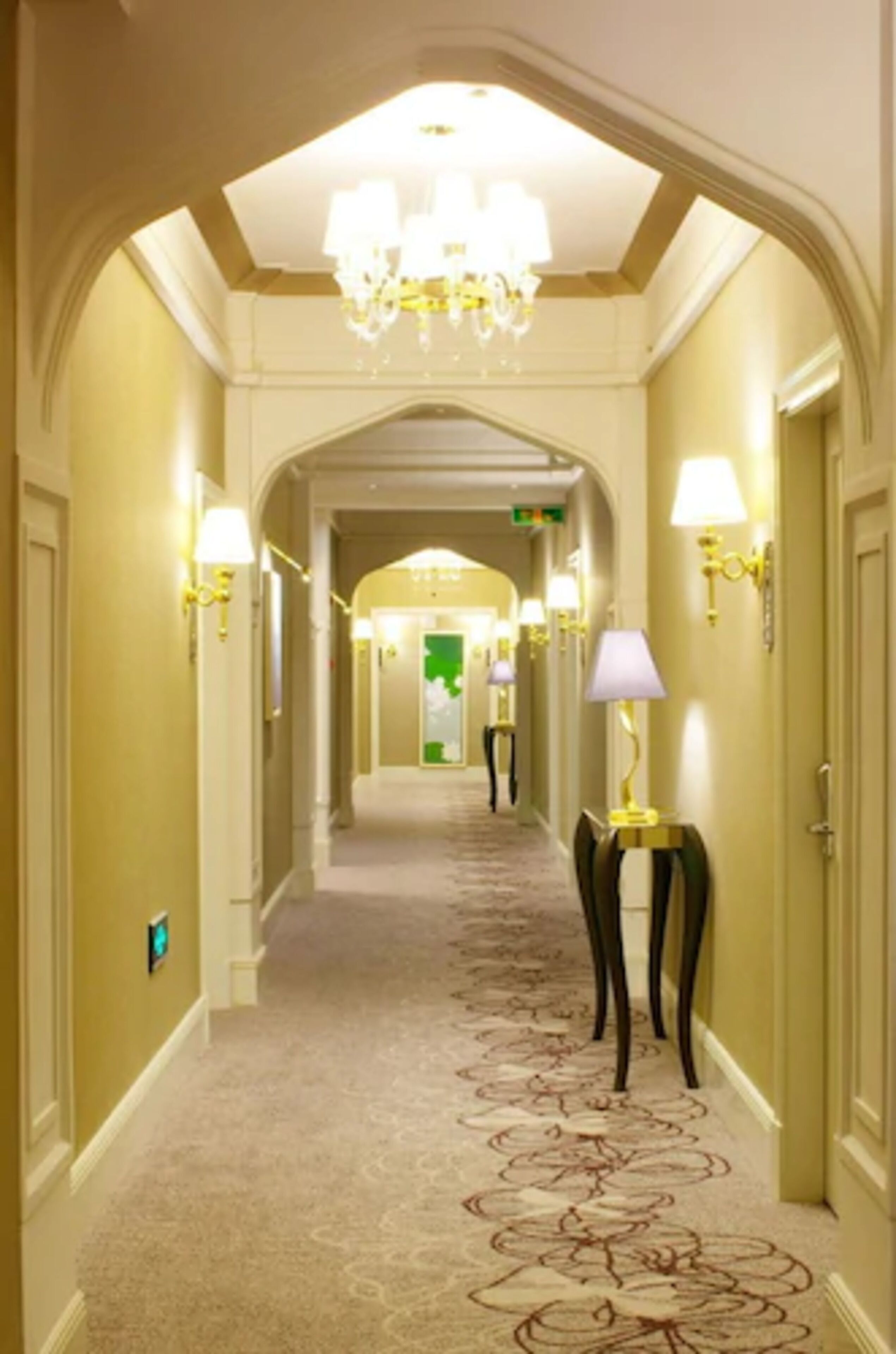 Un couloir d’hôtel doté d’un sol recouvert de moquette, de lustres, d’appliques murales et d’un plafond en arc de cercle.