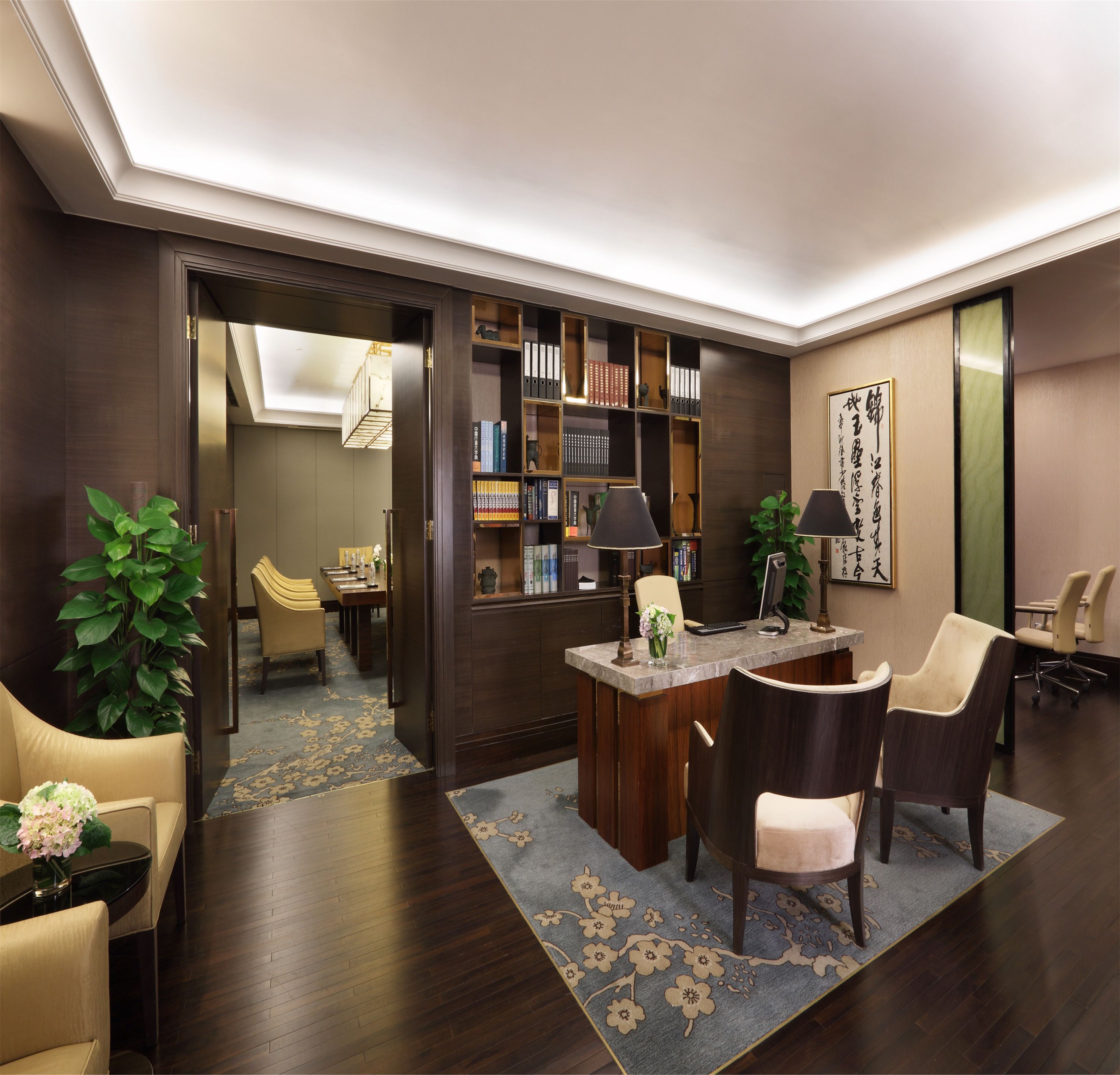 A modern, well-lit living room with a wooden floor, a central coffee table, and a bookshelf filled with books and decorative items.