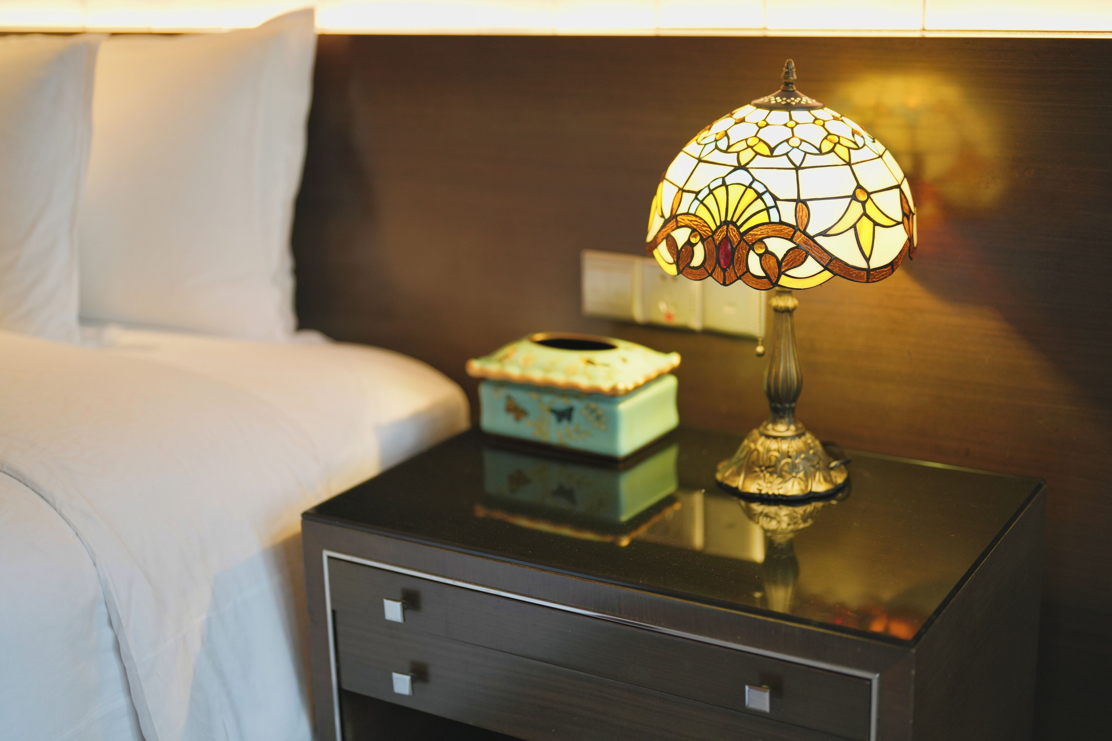 A bedside table with a lamp, a small decorative box, and a drawer.