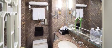 Un baño moderno con pared de mármol, inodoro blanco, lavabo con encimera de vidrio y un espejo grande.