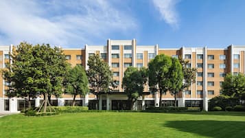 Een hotel met meerdere verdiepingen, een centraal gelegen ingang, omringd door een verzorgd gazon en bomen.