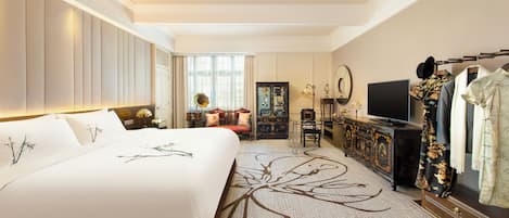 Quarto de hotel com cama grande, televisão, guarda-roupa e secretária com luminária.